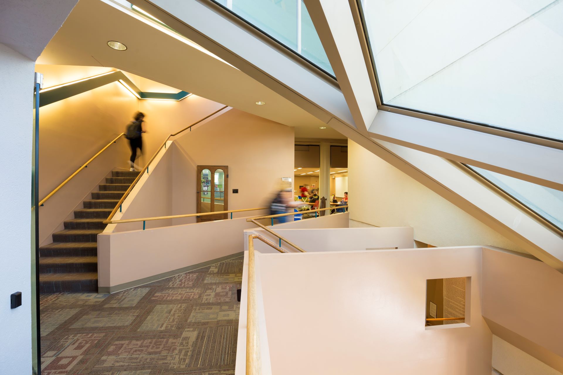 Modern university building interior with geometric windows, beige walls, and students using the staircase